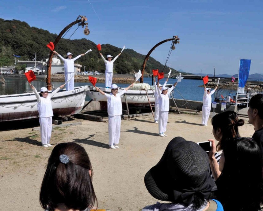 粟島に到着した観客を手旗信号で出迎える演者ら＝三豊市詫間町