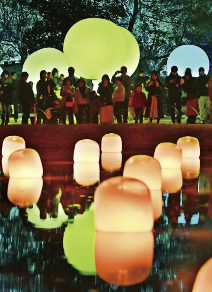 池に浮かぶカラフルな光を放つアート作品に見入る入場者＝高松市の栗林公園
