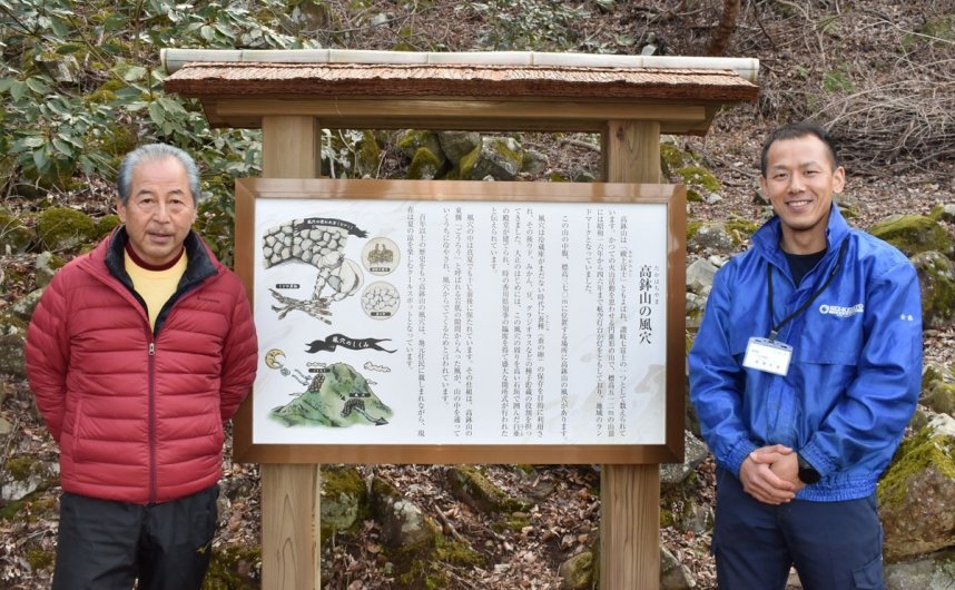 高鉢山風穴の近くに整備した解説板と、設置に取り組んだ金盛さん（右）、山下さん＝香川県綾川町西分