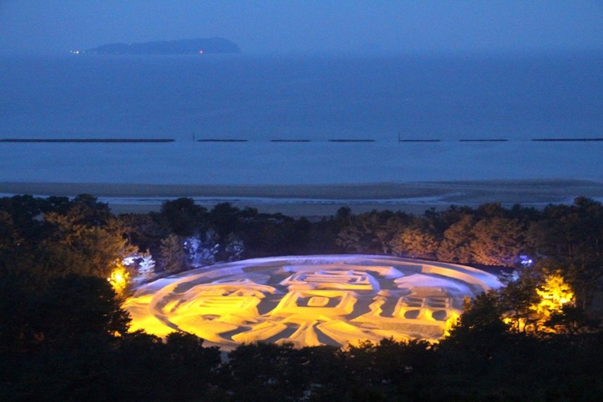 ウクライナ国旗の色の青と黄色にライトアップされた銭形砂絵「寛永通宝」＝香川県観音寺市有明町