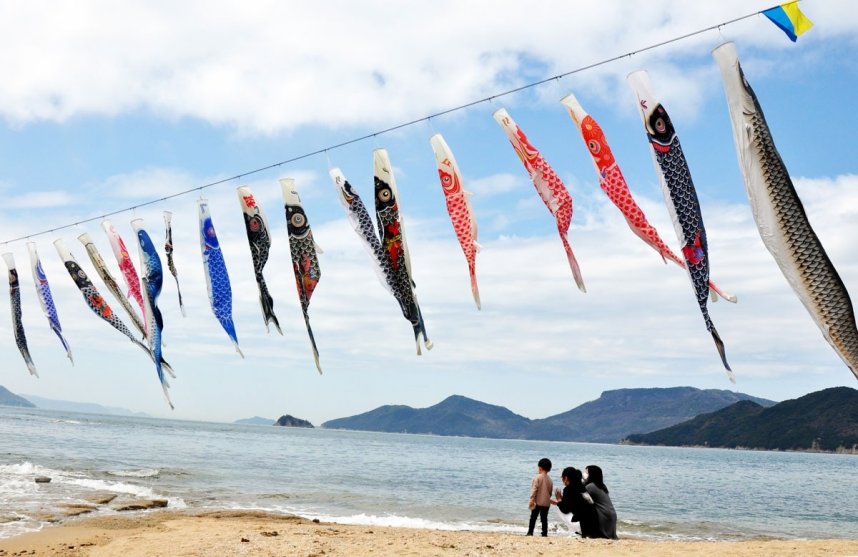 潮風に揺れるこいのぼりを見上げる家族連れ＝香川県土庄町、戸形公民館前