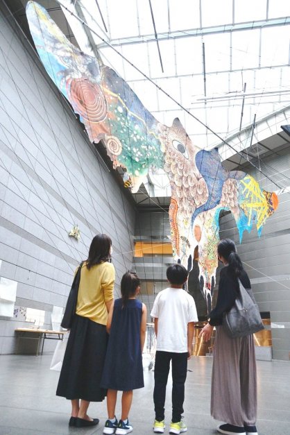 エントランスホールにつり下げられた新作「皮トンビ」を見上げる親子連れ＝香川県高松市紺屋町、市美術館
