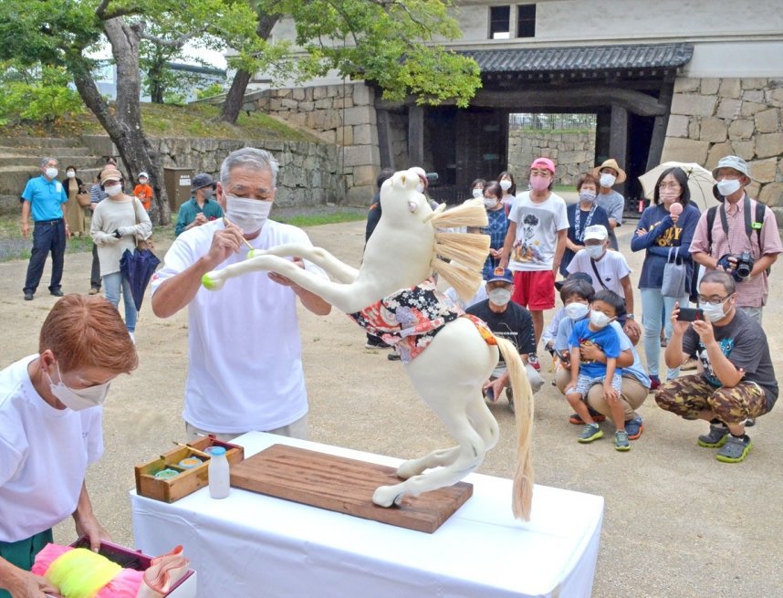 「八朔だんご馬」の制作実演で岡さん夫妻の作業を見守る家族連れら＝香川県丸亀市一番丁、丸亀城