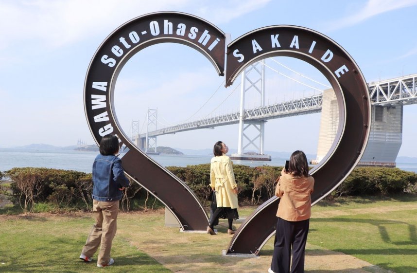 瀬戸大橋を背景に、完成したモニュメントの前で記念撮影を行う来園者＝香川県坂出市番の州緑町、瀬戸大橋記念公園