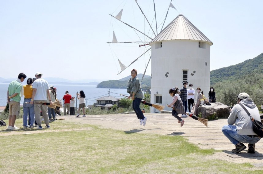 フォトスポットとして人気のギリシャ風車がある芝生広場。多くの観光客らが「魔女」になりきってほうきにまたがる＝２０２２年５月３日、香川県小豆島町西村の小豆島オリーブ公園