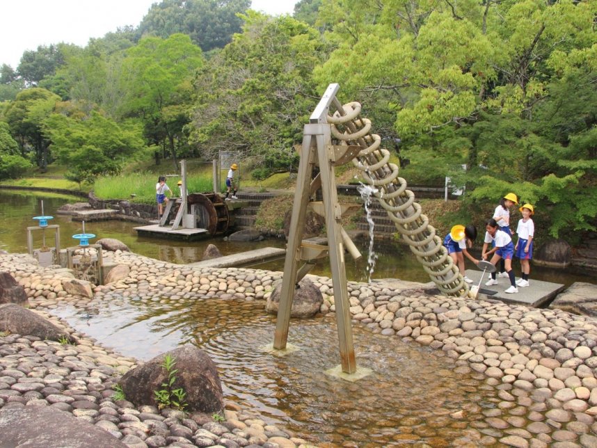 「じゃぶじゃぶ池」に設置された遊具「アルキメデスのポンプ」などで遊ぶ児童たち＝三豊市財田町、香川用水記念公園
