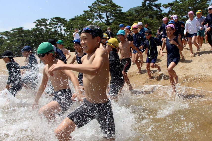 海開きを迎え、歓声を上げながら海に駆け込む児童たち＝２０２３年７月６日、さぬき市津田町の津田の松原海水浴場