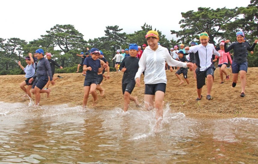 初泳ぎで勢いよく海に駆け込む児童たち＝香川県さぬき市津田町、津田の松原海水浴場