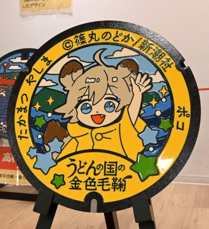 漫画「うどんの国の金色毛鞠」のキャラクターが描かれた高松市の新デザインマンホール＝香川県高松市、市民交流プラザＩＫＯＤＥ瓦町