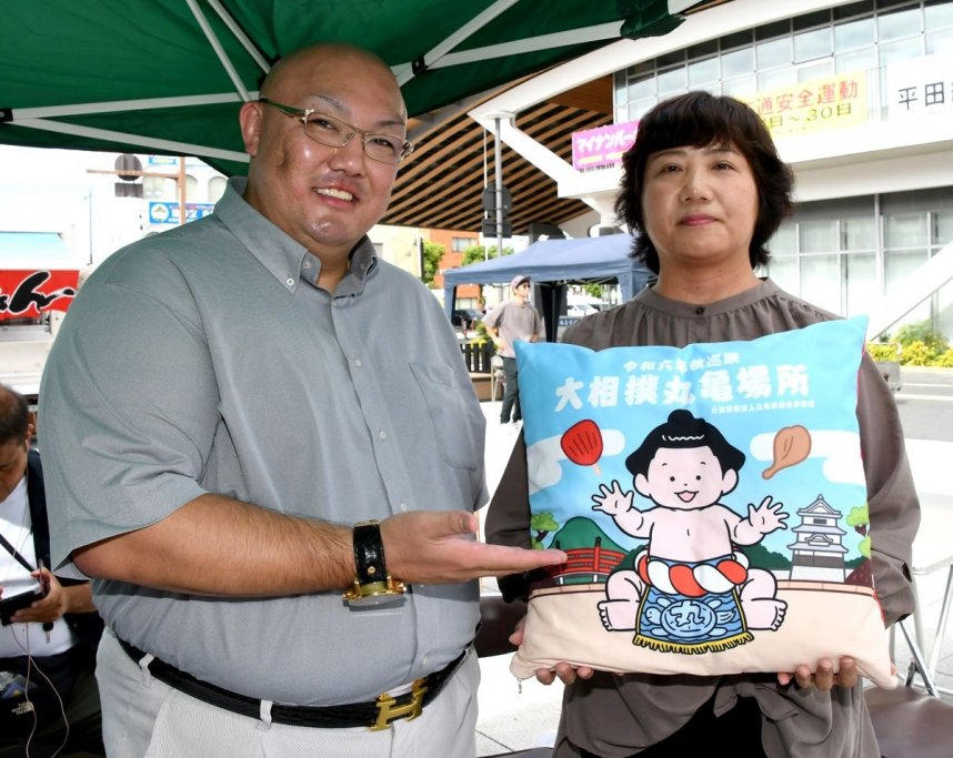 丸亀場所のキャラクターが描かれた座布団を手にする高木さん（右）。左は荒磯親方＝香川県丸亀市大手町