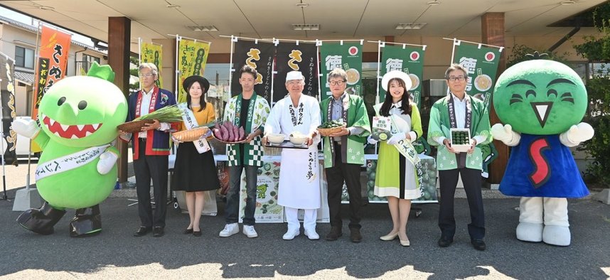 生産者から青ネギとサツマイモ、スダチを受け取った香川社長（中央）＝香川県高松市松縄町