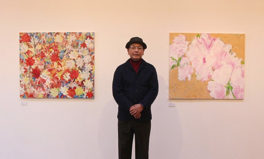 花や赤く色付いた葉を描いた作品とともに写真に納まる松村