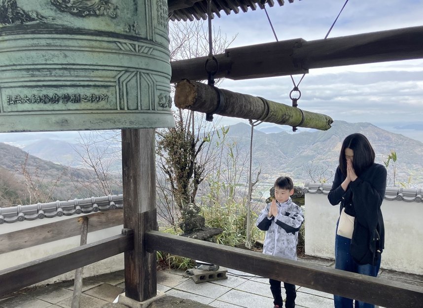 天空の鐘を突き手を合わせる参拝者＝香川県善通寺市吉原町